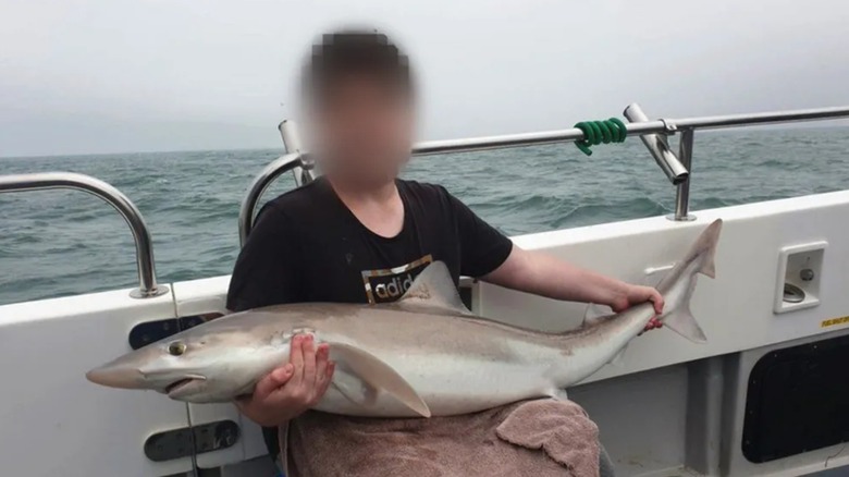 Arion Kurtaj with blurred face holding a fish on a boat