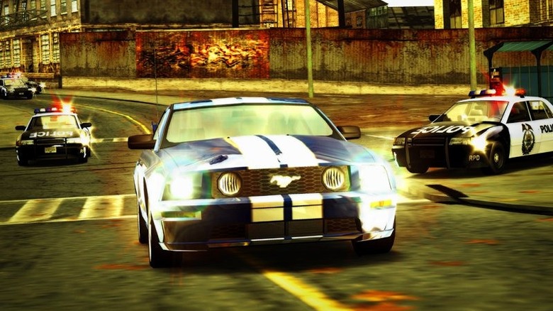 A blue Ford Mustang is chased by police cars through a city in Need for Speed: Most Wanted