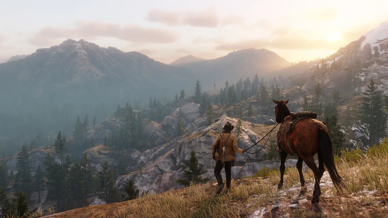 Arthur Morgan walks alongside his horse through a mountain range during sunrise in Red Dead Redemption II