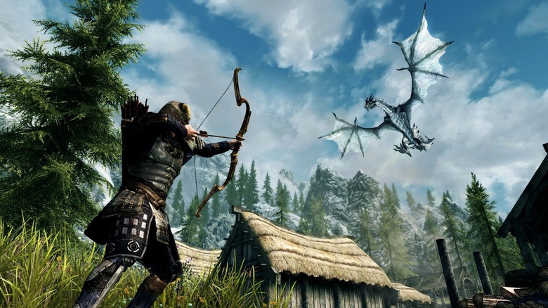 The player character aims an arrow at a dragon flying over a village in The Elder Scrolls V: Skyrim