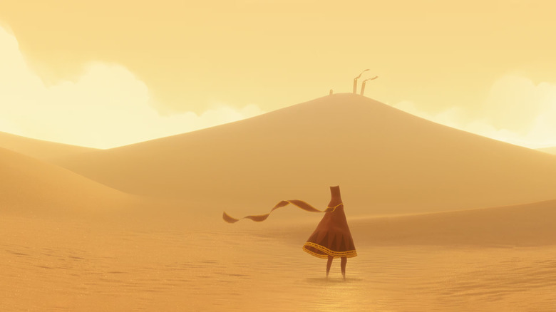 A cloaked figure walks through a desert towards two flags blowing on a dune in Journey