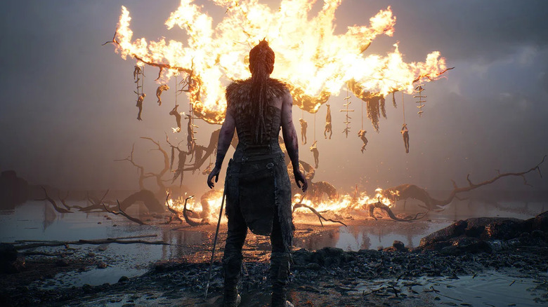 Senua faces a burning tree with bodies hanging from it in "Hellblade: Senua's Sacrifice" (2017)