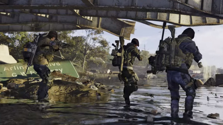 Three soldiers walk on a riverbank under a bridge in Tom Clancy's The Division 2