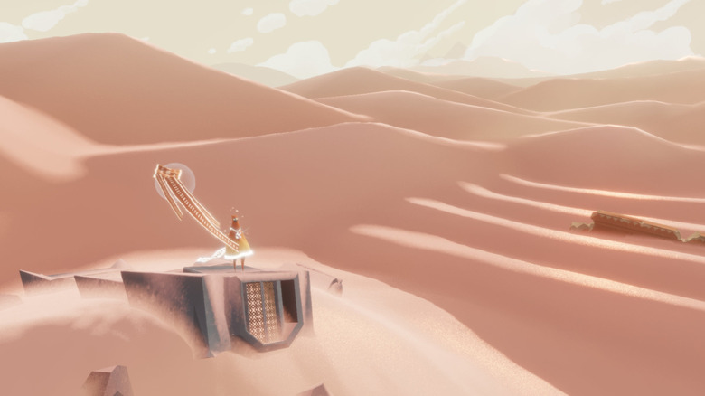 The player character surveys the desert as a flag flutters beside them in Journey (2012)