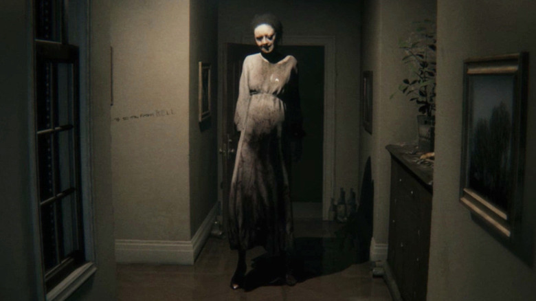 Lisa stands menacingly in the middle of a dark hallway in "P.T." (2014)