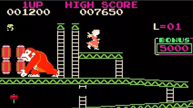 A gorilla reaches for a barrel while a woman stands on a platform beside him in Crazy Kong