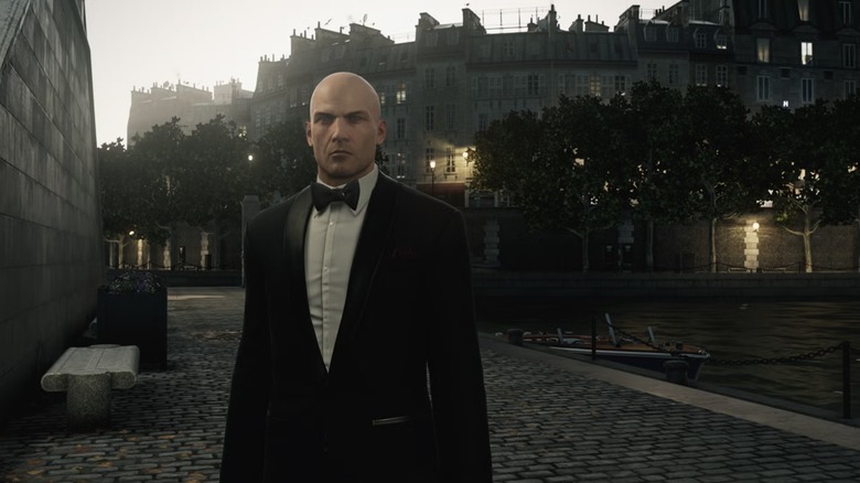 Agent 47 stands in a European city in a tuxedo in Hitman
