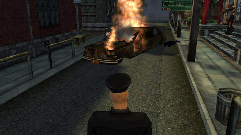 Agent 47 wearing a chauffeur uniform looks at a burning car in Hitman: Codename 47