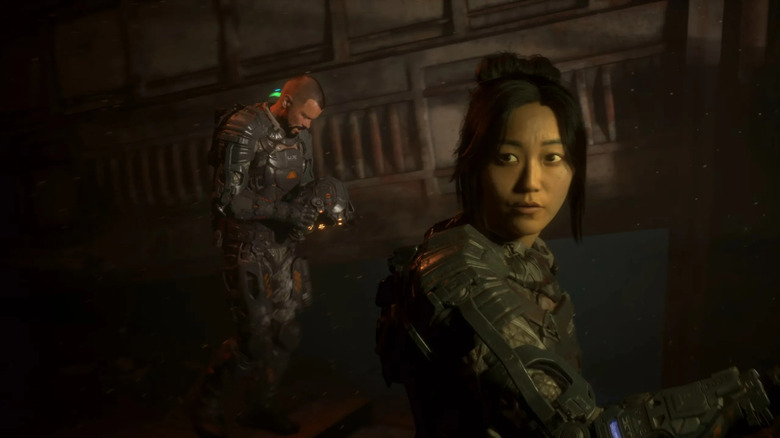 Dani Nakamura (Karen Fukuhara) looks up as Jacob Lee (Josh Duhamel) examines a helmet behind her in The Callisto Protocol