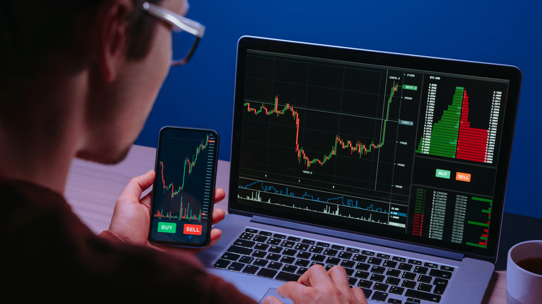 A person sitting at a computer and holding a phone while looking at stock information