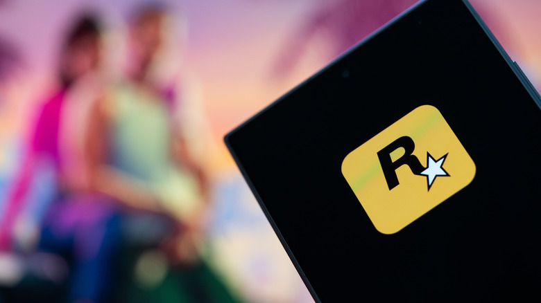 A phone with the Rockstar logo sits in front of a blurred background with GTA 6 art
