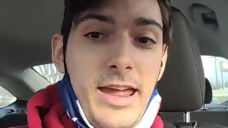 Ice Poseidon in a car with a mask pulled under his chin