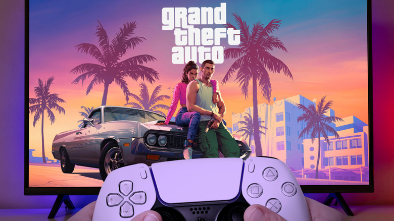 A hand holds a PlayStation 5 controller in front of a screen showing Grand Theft Auto VI